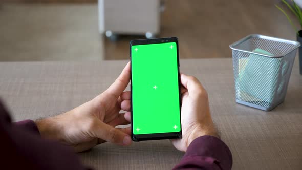 Male Hands Scrolling on Smartphone with Green Screen Chroma Mock Up at His Desk