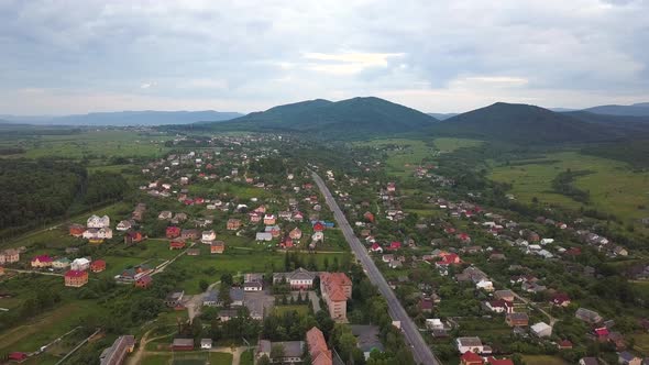 Aerial view of Nadvirna town with scattered small houses on green hills and distant Carpathian