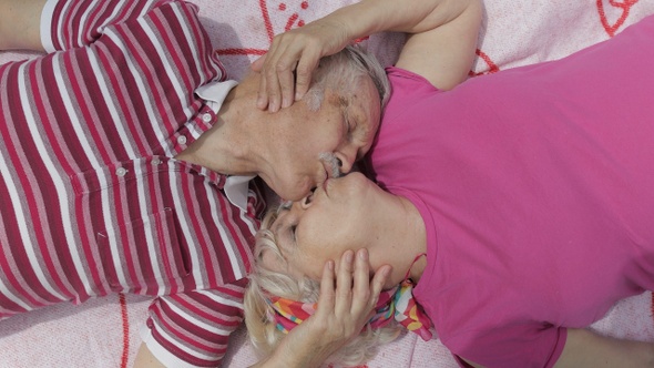 Family Weekend Picnic. Senior Old Caucasian Couple Lie on Blanket Facing Each Other, Making a Kiss