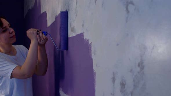 Close Up of Young Woman Painting Wall in Purple Colour with Roller