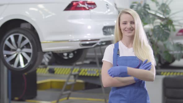 Middle Shot of Young Caucasian Woman Crossing Hands and Smiling. Blond Female Auto Mechanic Posing