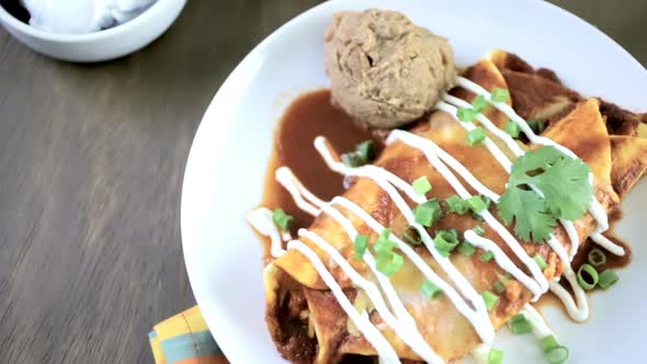 Dinner plate with Chicken enchiladas garnished with green onions and sour cream.