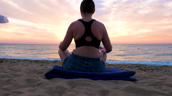 Woman Sits on the Beach Practicing Yoga at the Sunrise