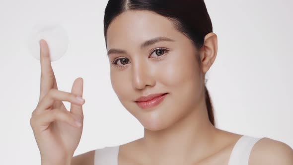 Attractive beautiful young Asian woman cleaning face with cotton pad isolated on white background.