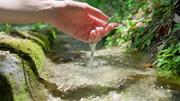 Hand touching flowing stream water.