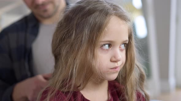 Closeup of Charming Beautiful Caucasian Little Girl Thinking As Blurred Man Making Hairstyle for