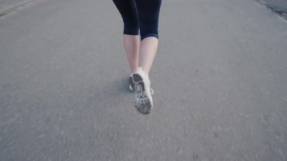 Close Up Woman Legs Running on Concrete Footpath at Public Park with Sunlight in the Background.