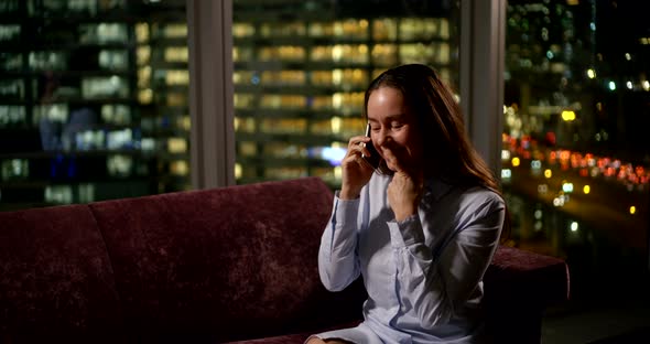 Cute Brunette Sitting and Talking on a Smartphone Near a Large Window. She Laughs a Lot and Gestures