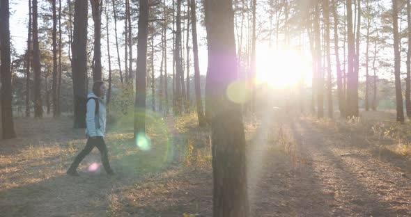 Young Tourist Girl in Bright Blue Jacket with Big Backpack Walking Through Fall Forest at Sunset