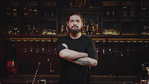 Barkeep Stands Behind Bar Counter and Crosses Arms Closeup