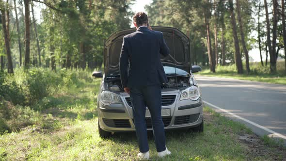 Back View Young Man Talking on Phone Calling Insurance Standing in Front of Broken Car with Open