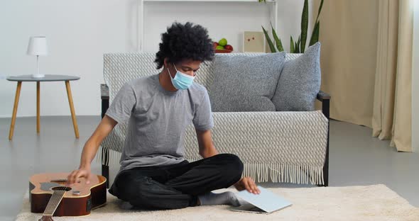 Afro American Teen Guy Black Man Sitting on Floor Wearing Medical Protective Mask Finishing Guitar