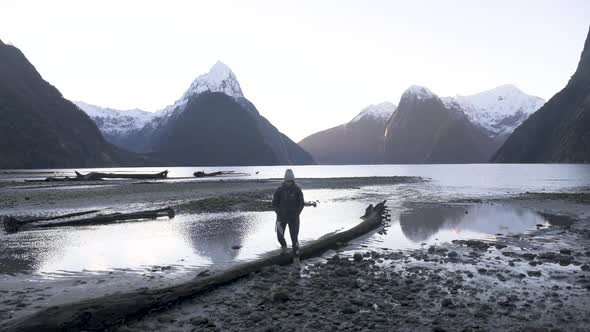 Slow motion shot of girl in hiking gear with camera walking along Milford Sound shoreline