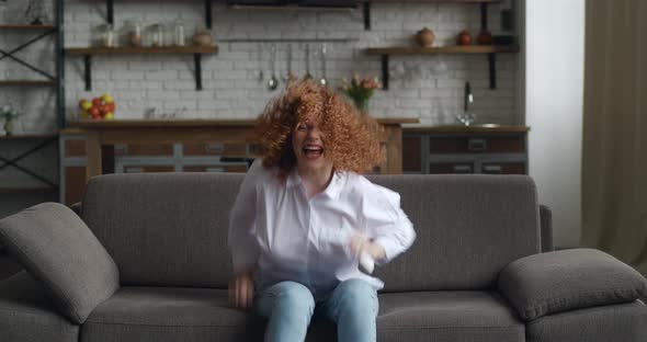 Excited Young Red Haired Woman Rejoices at Message on Her Smartphone While Sitting on Sofa at Home