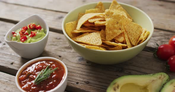 Close up of potato chips in a bowl, sauces and avocado on wooden surface