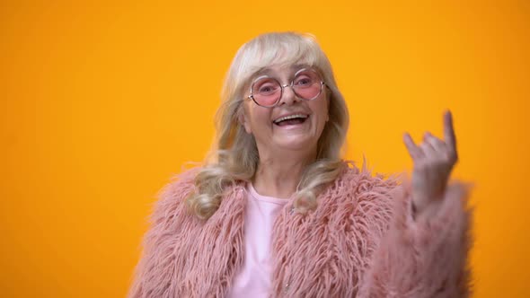 Joyful Elderly Lady in Funny Pink Clothes Making Rocker Gesture, Positiveness