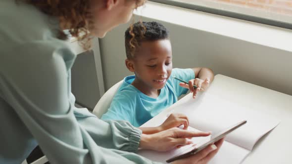 Video of happy caucasian female teacher explaining lesson on tablet to african american boy