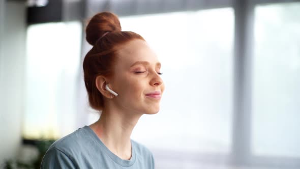 Close-up Face of Happy Carefree Redhead Young Woman Listening Music in Wireless Earphones at Home