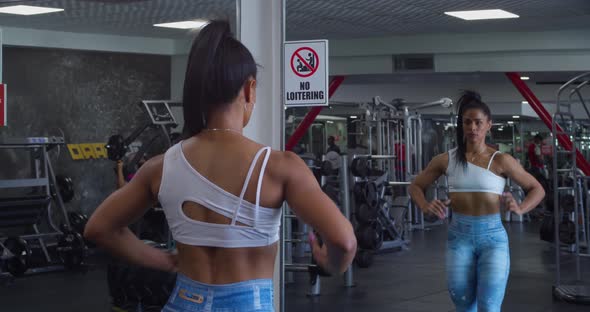 Female bodybuilder flexing her muscles with her mirror reflection at the gym