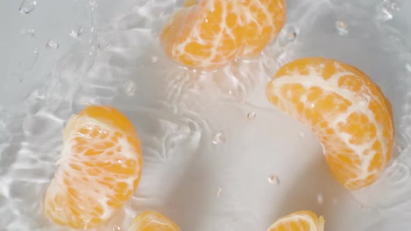Close up Peeled Mandarin orange Falls into Water breaks up into slices, white Background