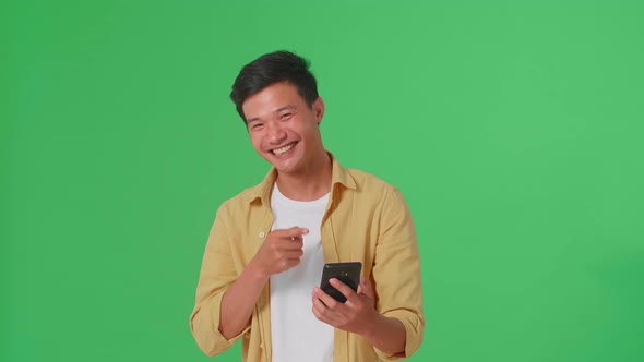 Smiling Asian Man Use Mobile Phone And Pointing To Smart Phone Screen In Green Screen Studio