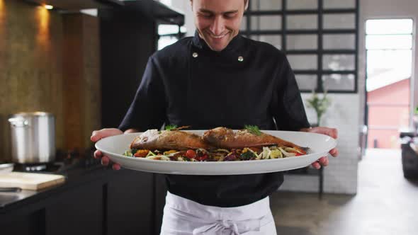 Caucasian male chef preparing a dish and smiling in a kitchen