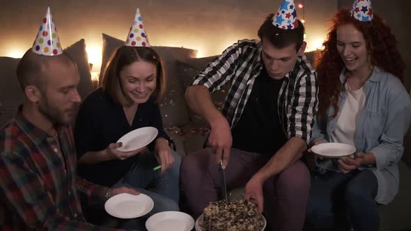 Birthday Guy in Plaid Shirt Cutting Festive Birthday Cake in Colorful Cone Hat