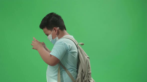 Boy Student Wearing A Mask And Playing Video Game On Mobile Phone While Walking On Green Screen