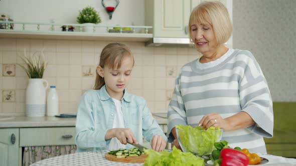 Happy Child Making Salad Then Doing High-five with Elderly Granny at Kitchen Table at Home