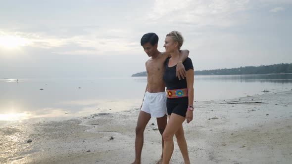 Young Thai Boy and Mature Caucasian Woman Couple Walking Together By the Sea at Sunset in Slow