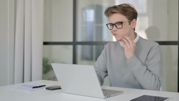 Young Man Having Toothache While Using Laptop in Modern Office