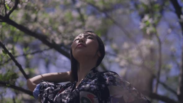Beautiful Asian Woman Dancing in Spring Blooming Sakura Garden in Sunlight