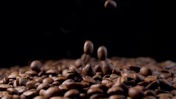 Roasted coffee beans with smoke. Slow motion of arabica coffee seeds falling.