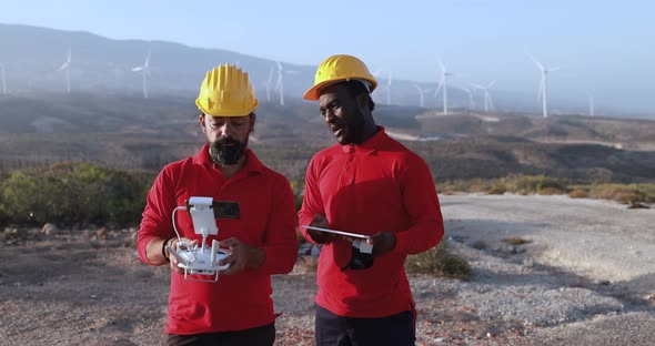 Multiracial engineer men working together on a windmill farm using digital tablet and drone - Renewa