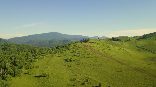 Aerial: Flying Over Sunny Fields, Under Clouds Along the Mountains. Also Visible: Forest, Tourists