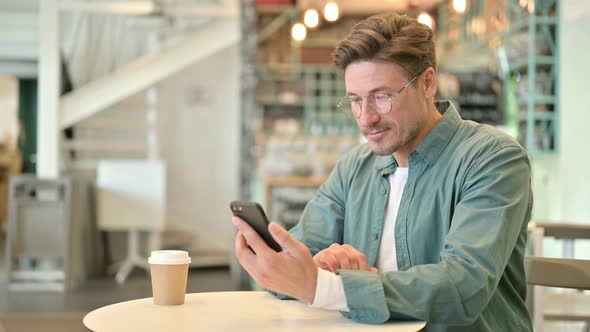 Attractive Middle Aged Man Using Smartphone in Cafe 