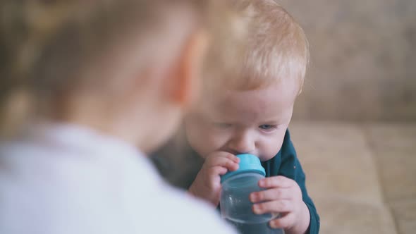 Little Baby Drinks Water From Bottle and Elder Sister on Bed