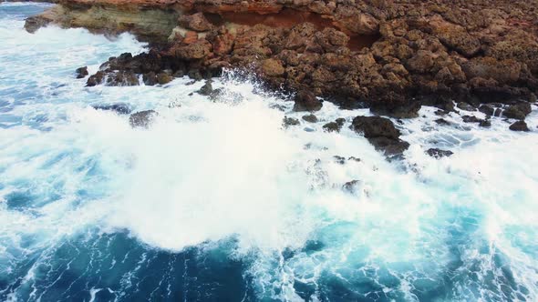 Sea Waves Washes the Rocky Shore Above Aerial Shot Flying Over Coastline Cliffside with Blue Pure