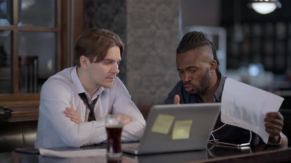 Focused Caucasian and African American Men Brainstorming Sitting in Restaurant Indoors