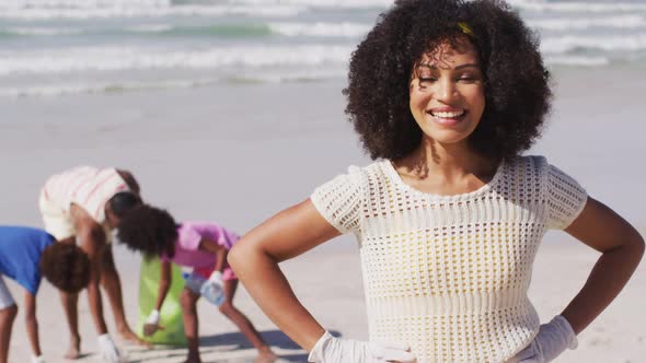 Portrait of african american mother, her family collecting rubbish and bottles from the beach