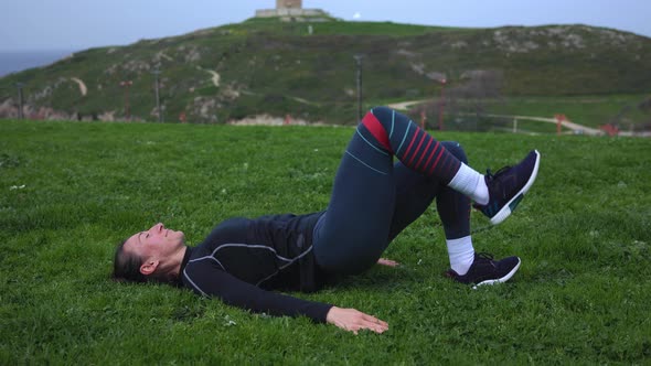 a Girl in Blue Leggings Lying on Green Grass and Doing Exercises with Rubber for the Buttocks