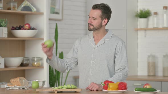 Young Man Showing Thumbs Up While Holding Apple in Kitchen