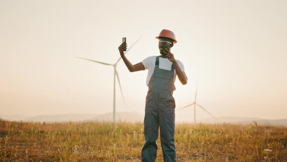 Positive Engineer in Uniform and Helmet Using Modern Smartphone for Video Call