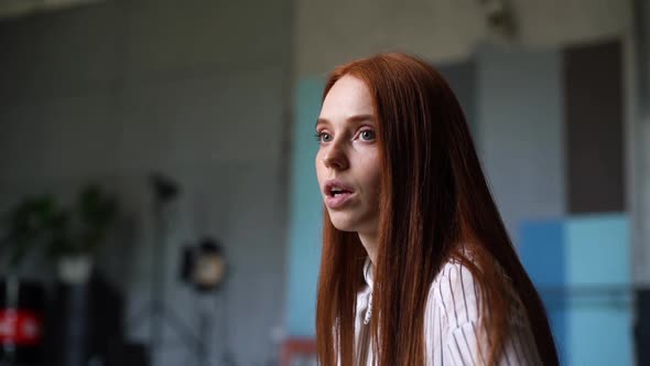 Close-up Face of Happy Attractive Young Woman with Red Hair Talking with Somebody at Office Room.