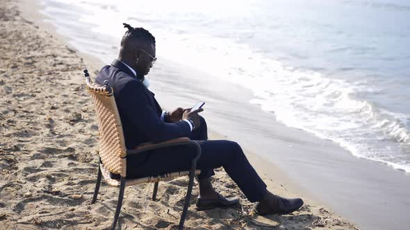 Side View of Absorbed African American Elegant Man Sitting on Chair Texting on Smartphone with Foamy