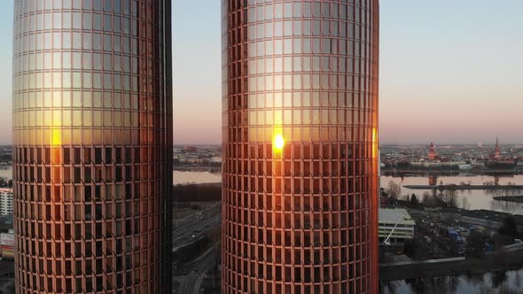 Sideway aerial drone view of two high rise glass office towers reflecting golden sunset on windows w