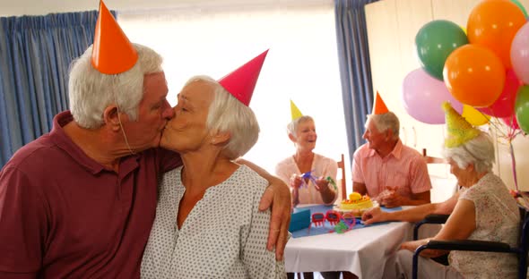 Senior couple kissing and hugging while celebrating birthday with friends