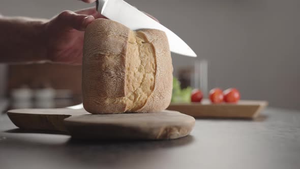 Man Slicing Small Ciabatta Bun for Sandwich on Kitchen Countertop