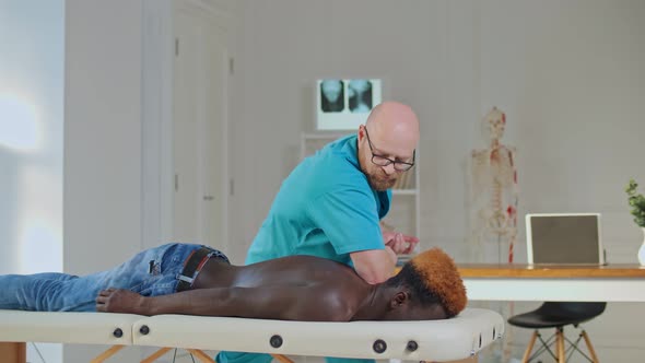 A Physical Therapist Is Giving Massage Therapy To a Black Man Who Is Lying on a Couch