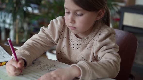Focussed little girl sitting at table doing homework